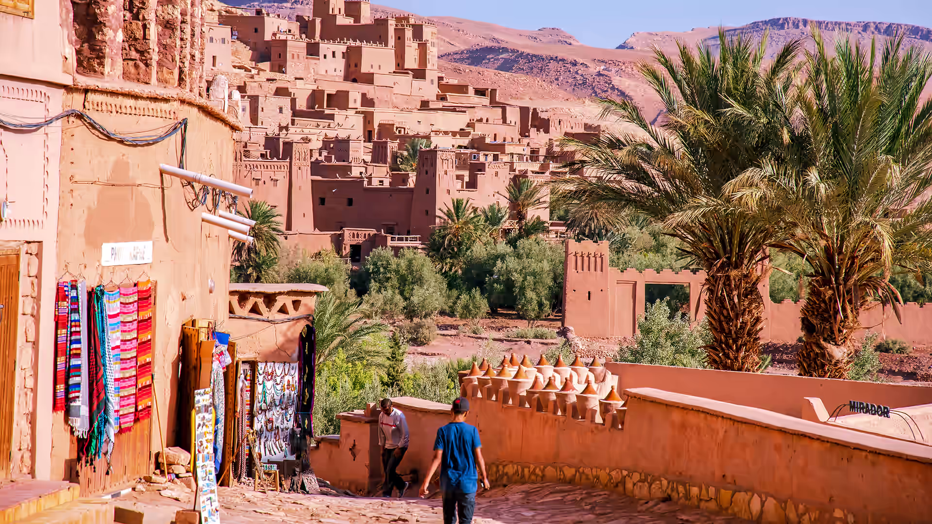 Calle de entrada a Ait Ben Haddou con tiendas de artesanía y palmeras