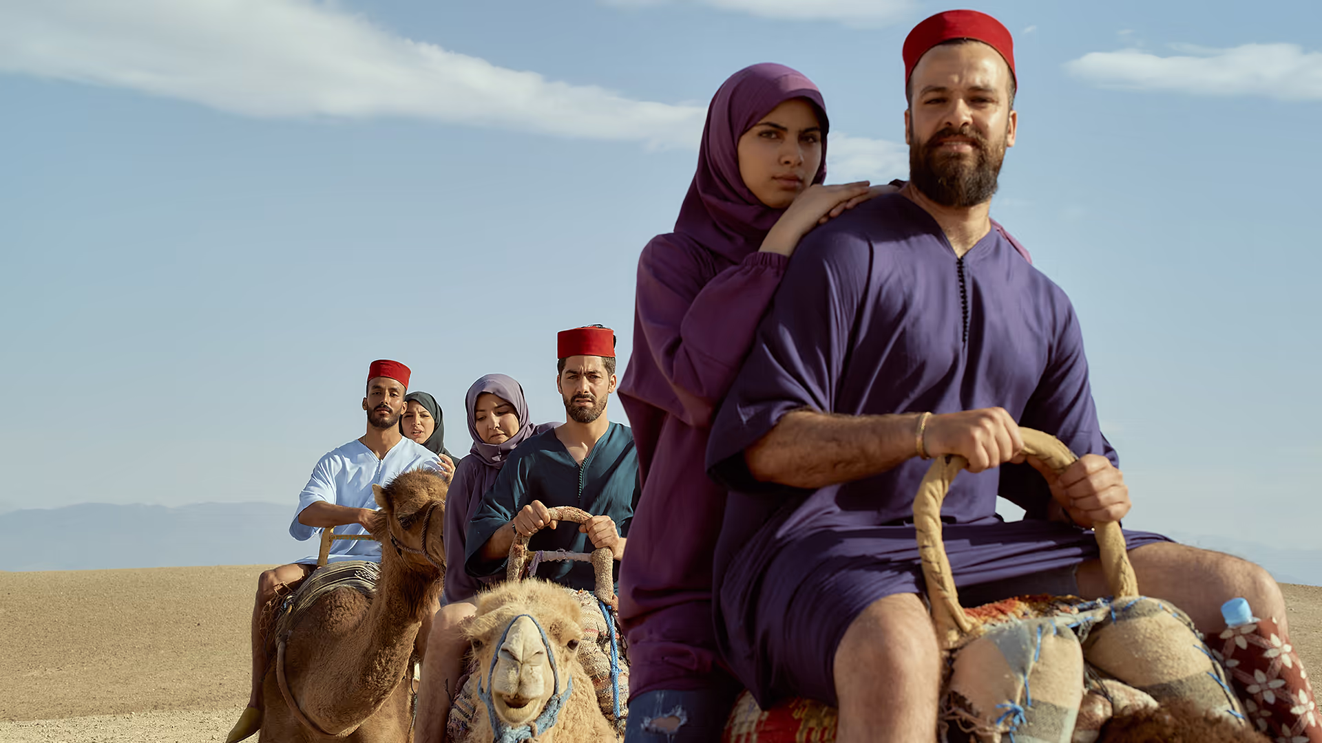 Grupo de viajeros con ropa tradicional montando en camello por el desierto